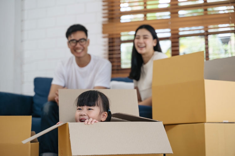 A family surrounded with moving boxes and a little girl sitting in one of the boxes