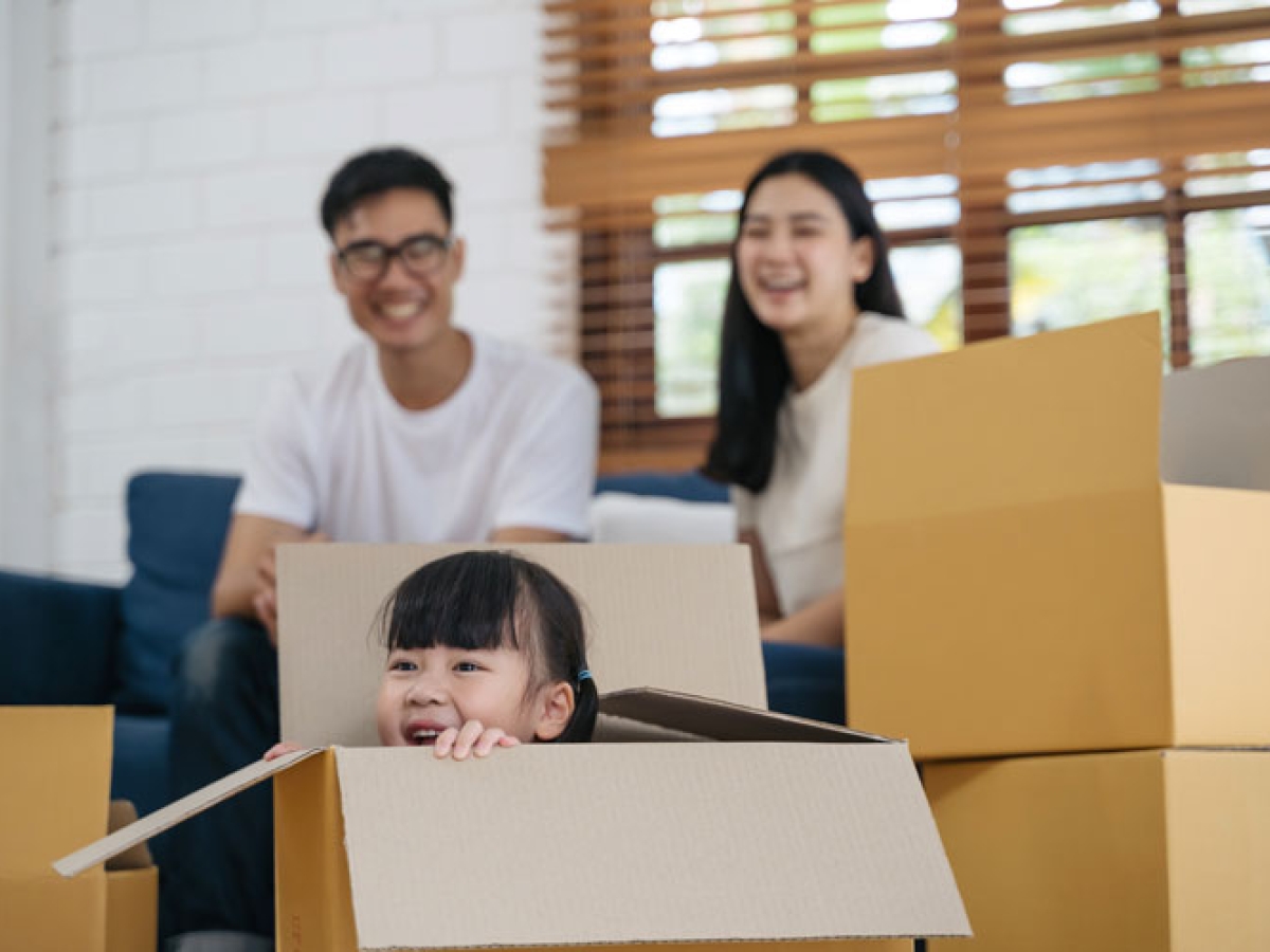 A family surrounded with moving boxes and a little girl sitting in one of the boxes