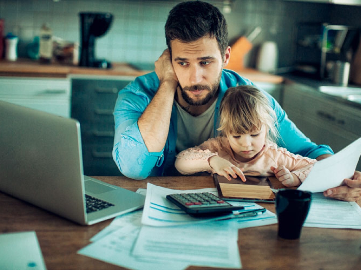 A man with his son sitting on his lap. He is looking at a laptop with a concerned look on his face. 